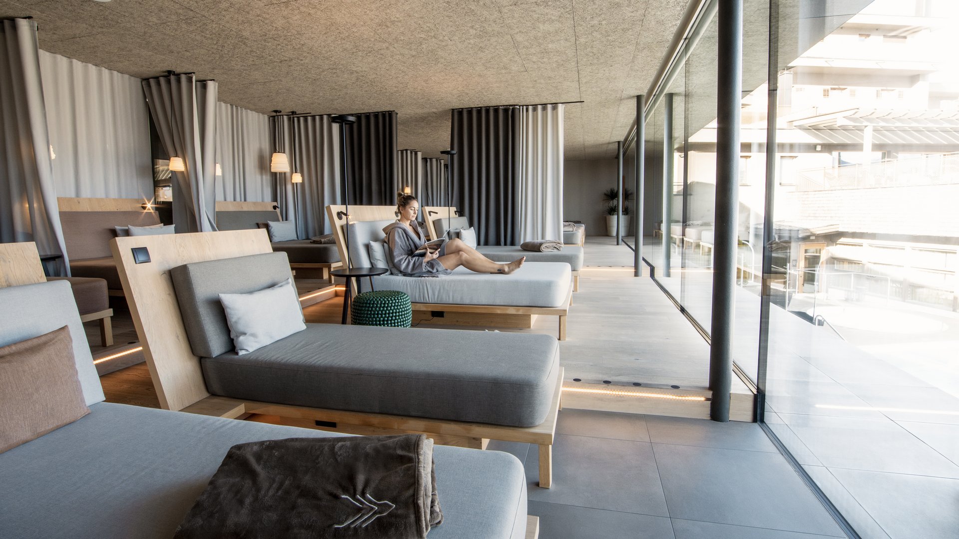 Our sauna, Plan de Corones/Kronplatz in full view Woman relaxing on lounge chair in modern quiet room with large windows