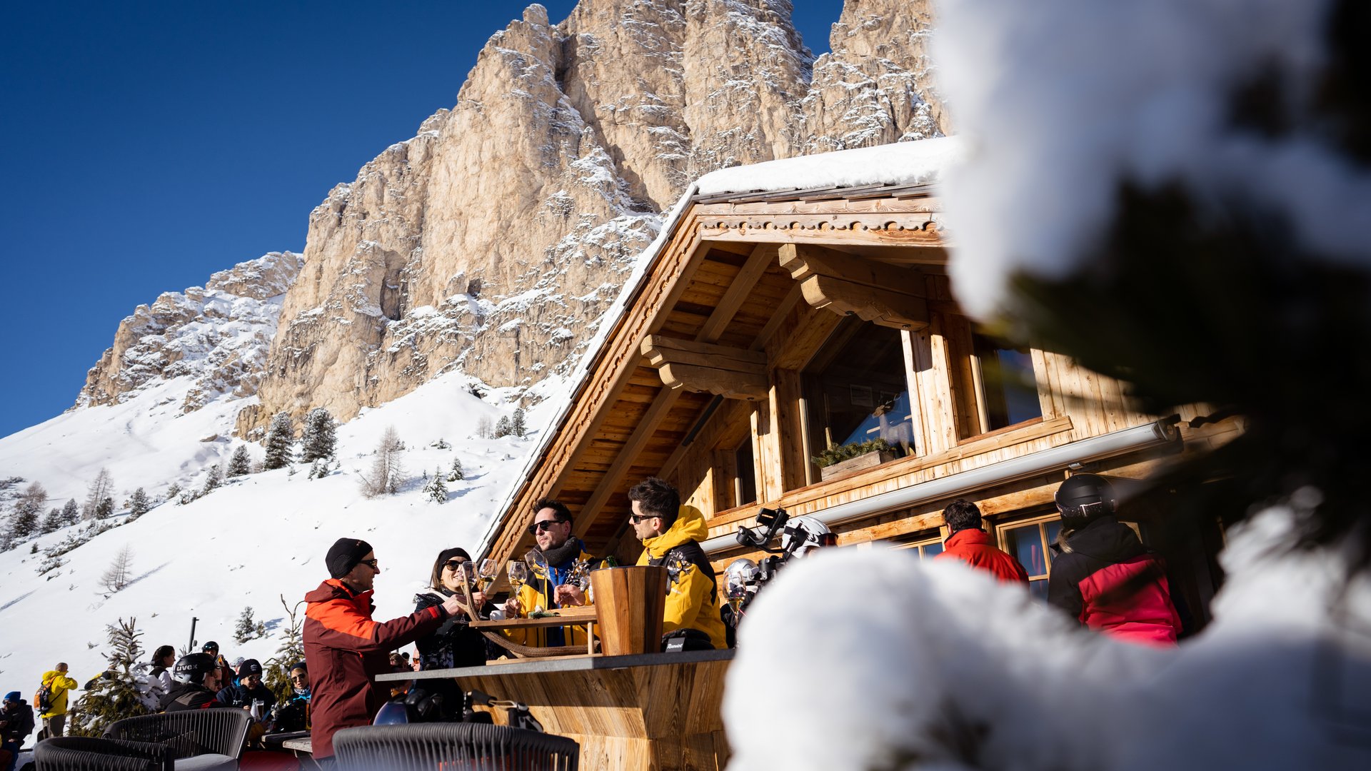 The best hotel at Plan de Corones/Kronplatz People enjoying drinks on terrace in front of snowy mountain cabin in winter
