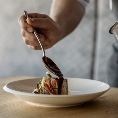 Vacanze in Alto Adige in estate: indimenticabili Cuoco versa salsa su un piccolo pezzo di carne su un piatto bianco