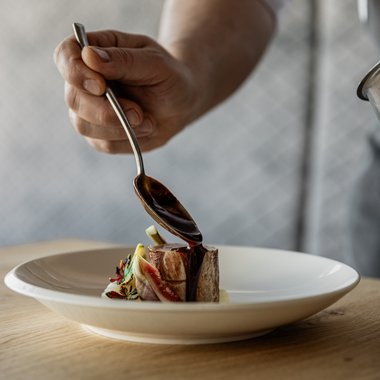 Shopping a Brunico e molto altro ancora Cuoco versa salsa su un piccolo pezzo di carne su un piatto bianco