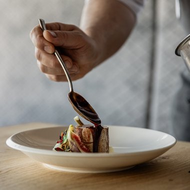 The Hubertus in a short time-lapse Chef pouring sauce over a small piece of meat on a white plate