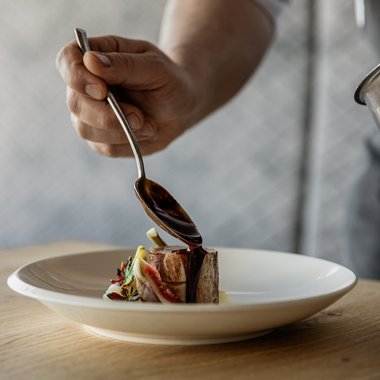 Bruneck: shopping & more Chef pouring sauce over a small piece of meat on a white plate