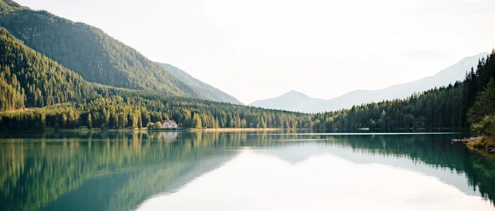 Unser aktueller Katalog zum Downloaden Bergsee mit reflektierenden Bäumen und einem Haus am Ufer