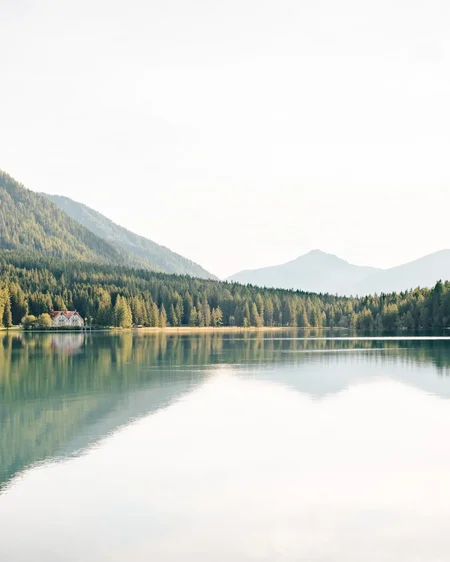 Unser aktueller Katalog zum Downloaden Bergsee mit reflektierenden Bäumen und einem Haus am Ufer